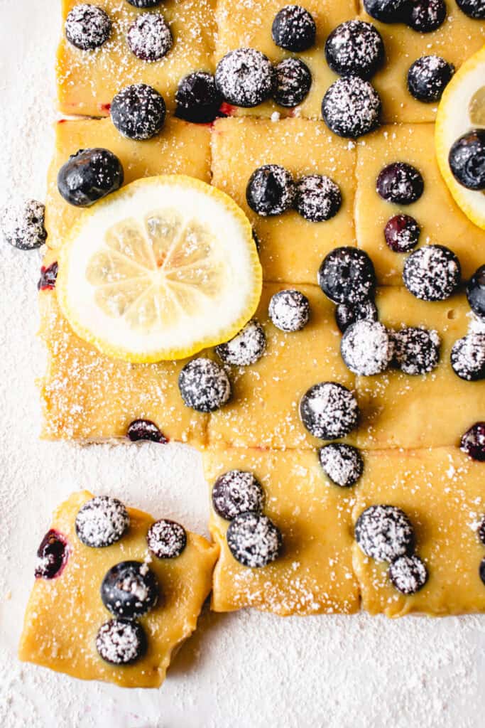 Gluten Free Lemon Blueberry Bars sliced into squares and garnished with lemon slices and sifted powdered sugar.