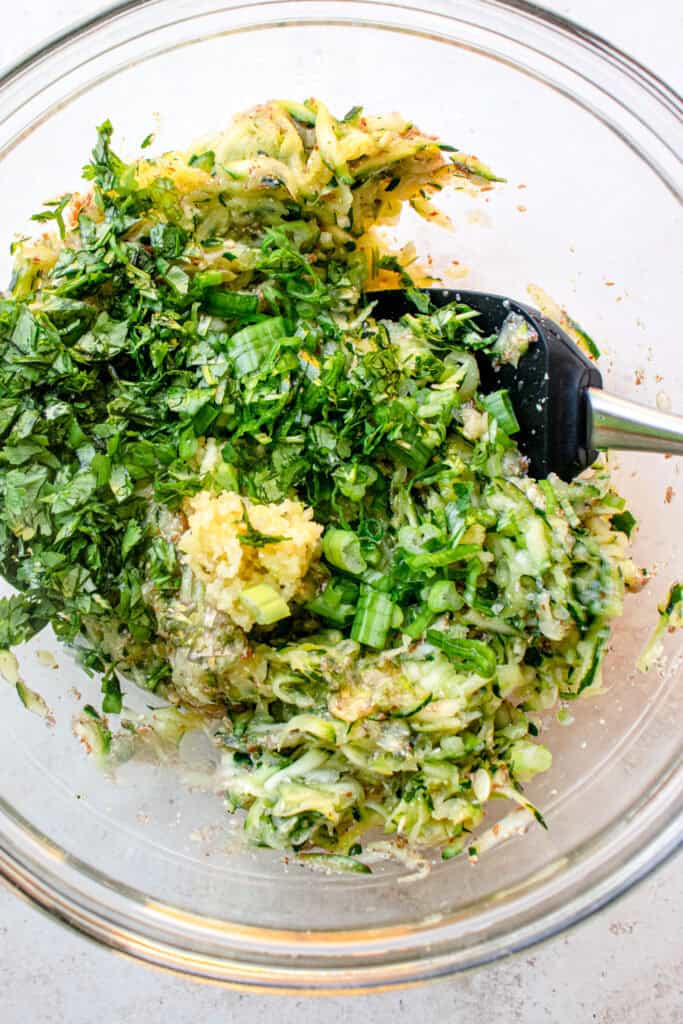 A large bowl with shredded zucchini, chopped cilantro, green onions, garlic, and lemon zest.
