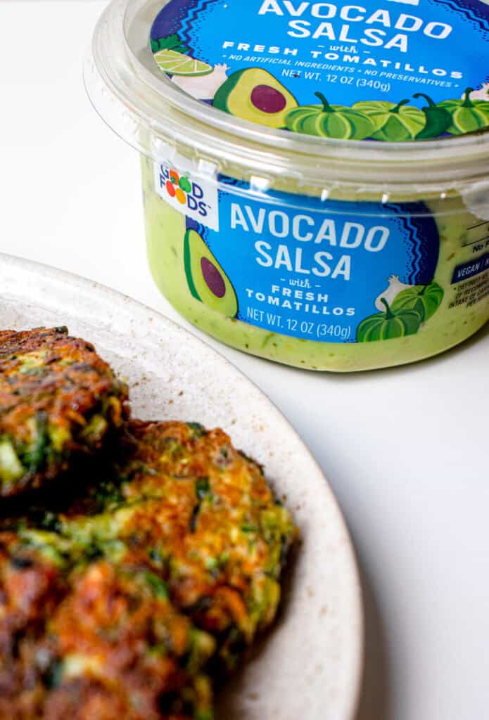 A plate with Gluten Free Zucchini Fritters and a container of Good Foods Avocado Salsa.