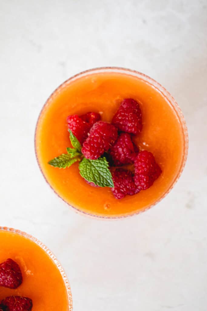 Overhead shot of two glasses of Easy Cantaloupe Dessert garnished with fresh raspberries and fresh mint leaves.