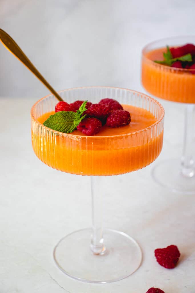Two glasses of Easy Cantaloupe Dessert garnished with fresh raspberries and fresh mint leaves.