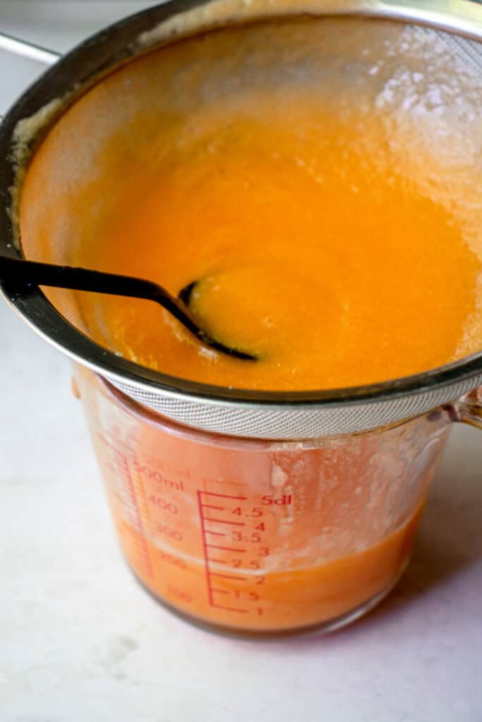 Puréed cantaloupe being strained through a mesh sieve to make cantaloupe juice.