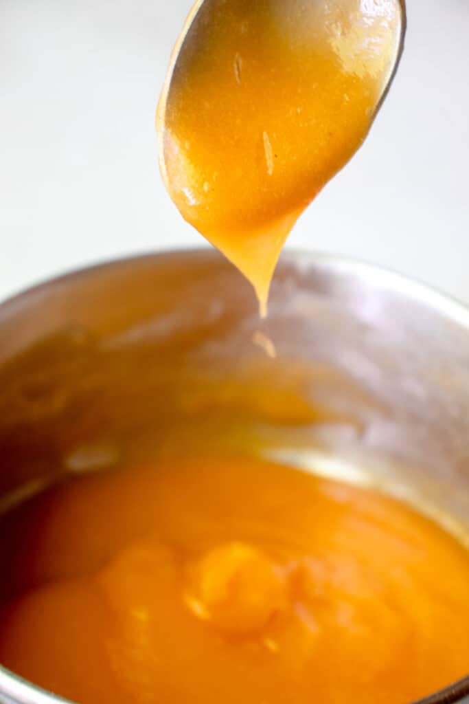 Closeup of a spoonful of thickened cantaloupe pudding scooped out of the saucepan.