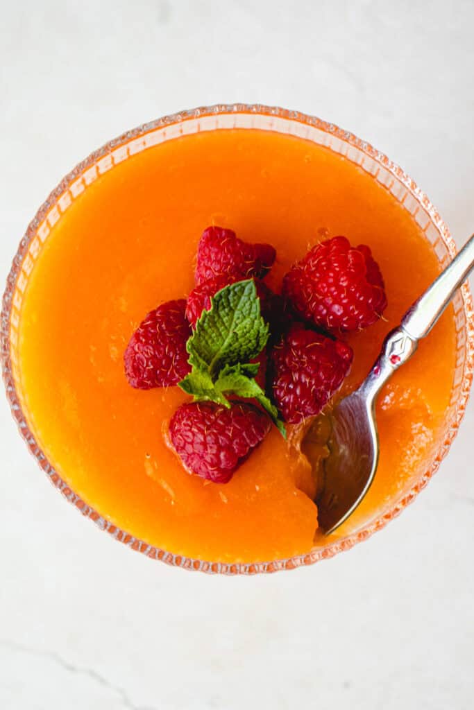 Overhead shot of a glass with the Easy Cantaloupe Dessert garnished with fresh raspberries and fresh mint.