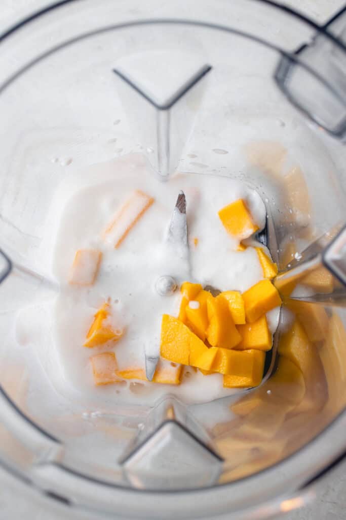 A blender with ripe mango cubes and coconut milk, before puréeing.