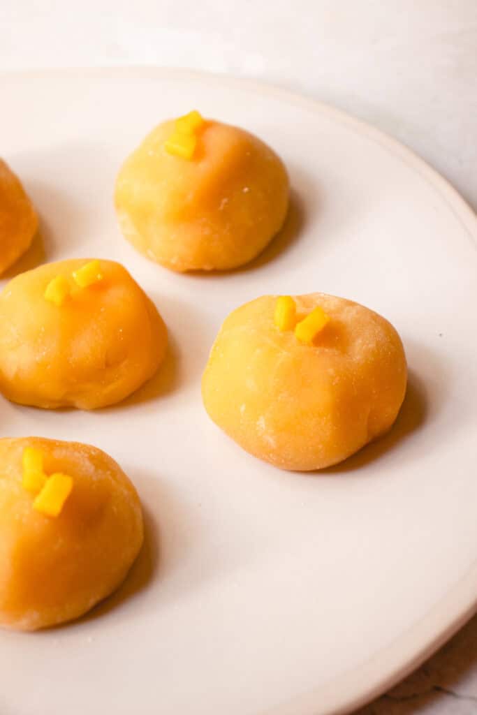 A plate with 5 pieces of Mango Mochi each topped with small pieces of fresh mango.