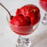 Two glasses with scoops of No Churn Raspberry Sorbet with Oranges, garnished with lime zest and olive oil.