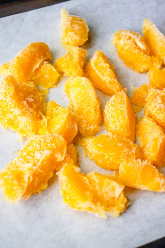 Frozen, segmented oranges laid flat on a parchment paper-lined sheet pan.