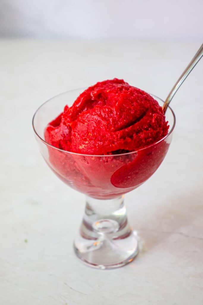 A serving glass with a scoop of the homemade orange-raspberry sorbet and a spoon.