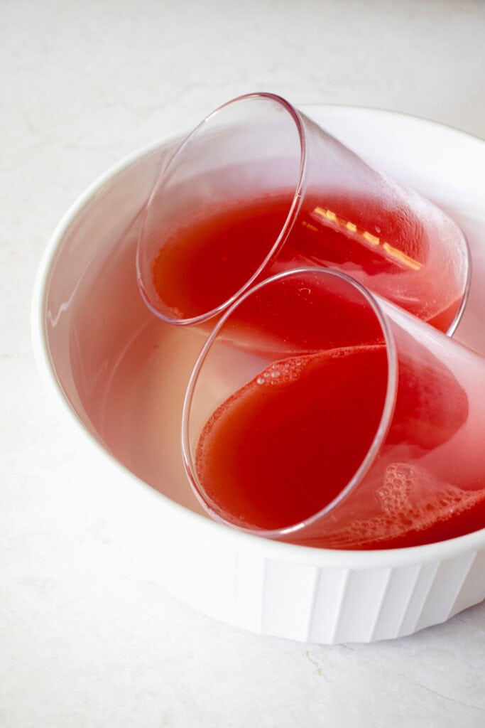 Watermelon gelatin mixture poured into two glasses, slanted, inside a round dish.