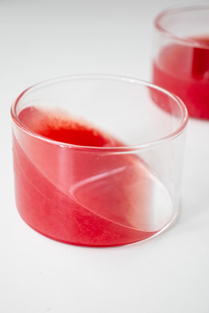 Two clear ramekins with watermelon jello set at an angle.