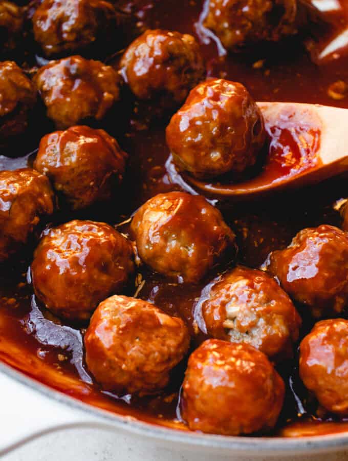 Baked meatballs coated in sweet and sour sauce in a pan with a wooden spoon.