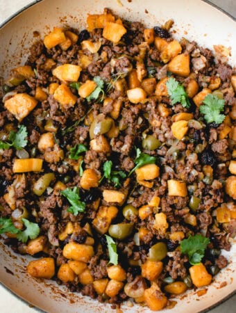 Plantain and beef hash garnished with fresh cilantro in a pan.