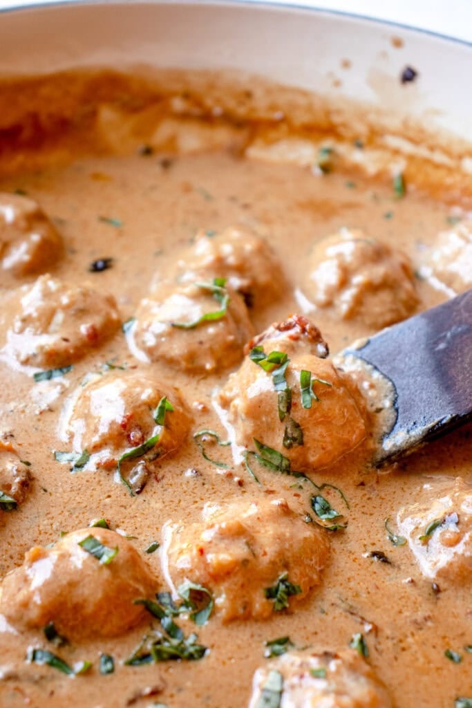 Overhead of a skillet with marry me chicken meatballs garnished with fresh basil.