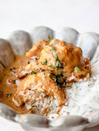 Small bowl with marry me chicken meatballs served over white rice.