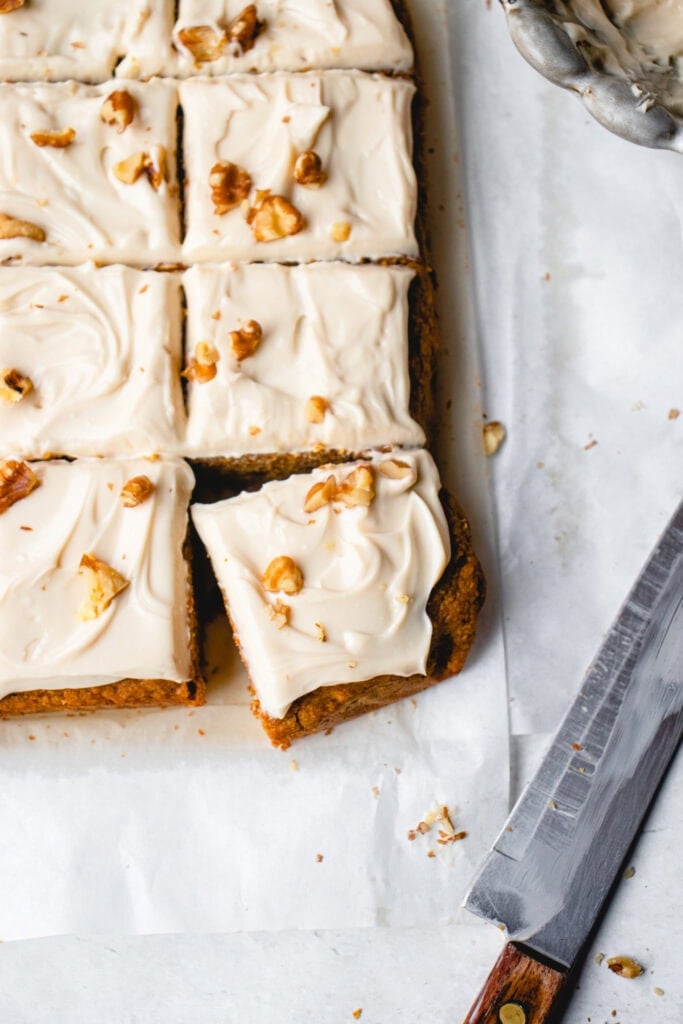 Cake cut into squares on top of parchment paper with a large knife at the side.