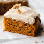 Close up of a square of carrot cake, frosted and topped with walnuts.
