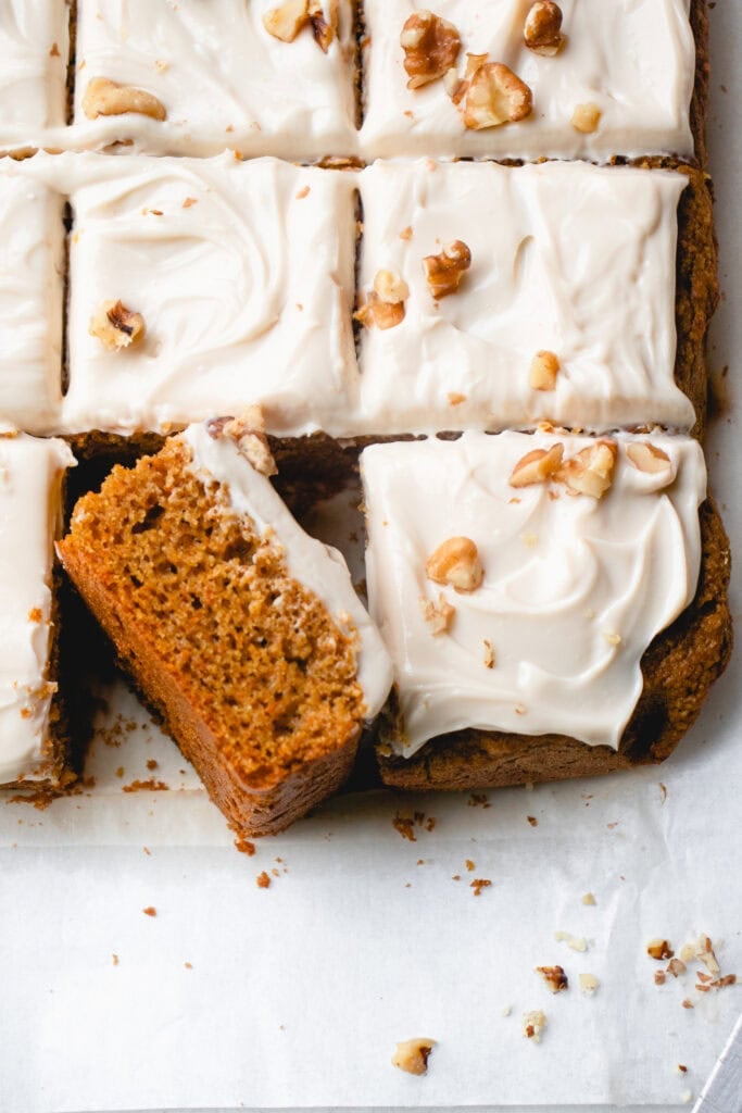 Overhead view of squares of frosted carrot cake with bottom left piece on its side.