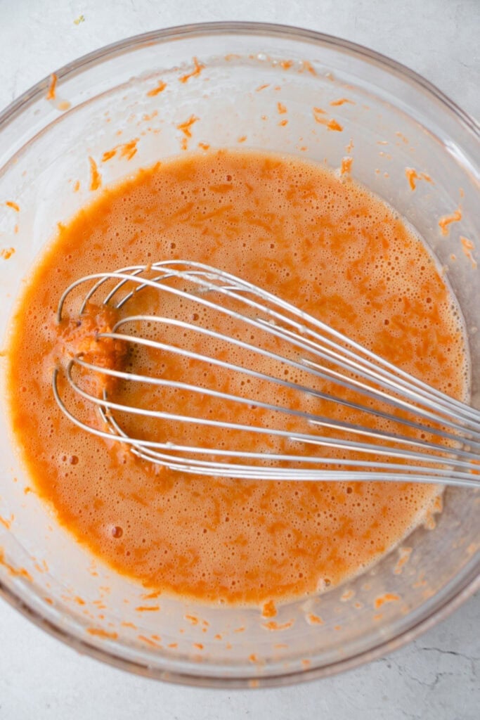 Large glass bowl with wet ingredient mixture and a whisk.