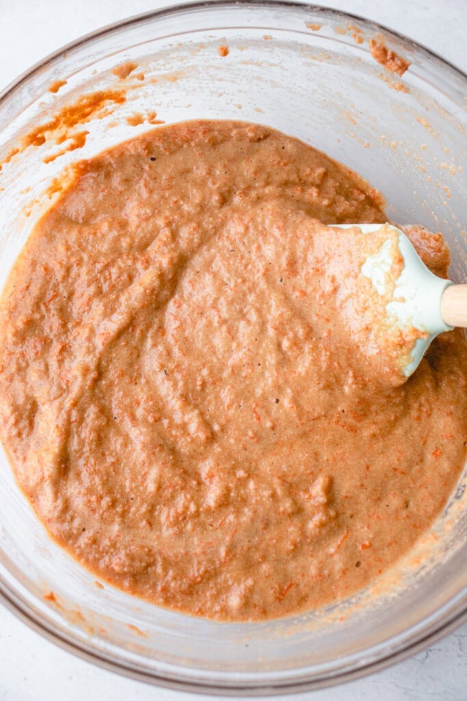 Large glass bowl with combined carrot cake batter and a spatula.