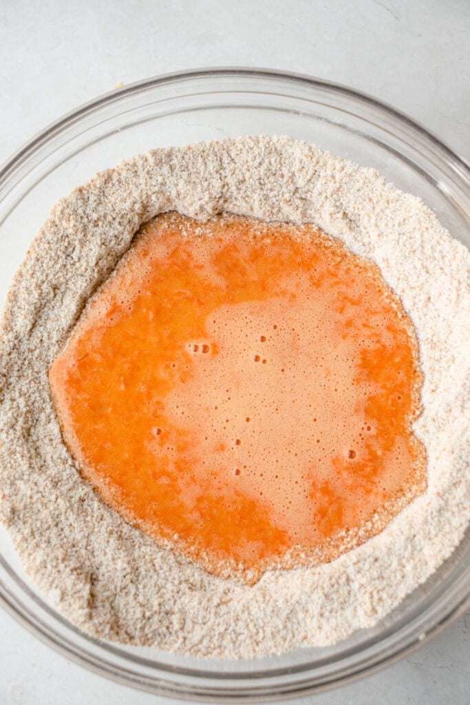 Large glass bowl with wet ingredient mixture poured into middle of dry ingredients.
